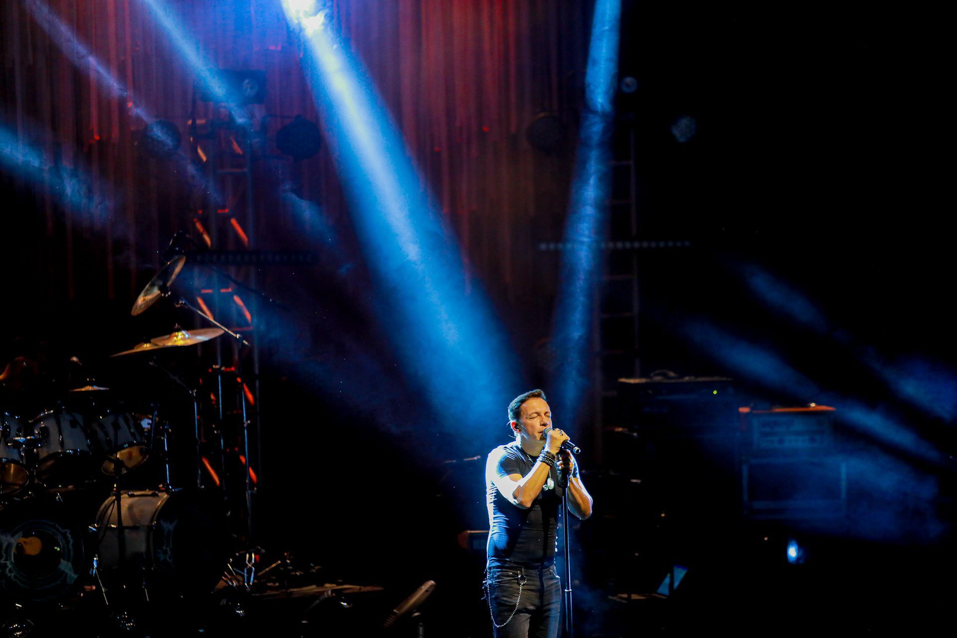 Um artista cantando em um microfone em um palco iluminado por holofotes azuis brilhantes.