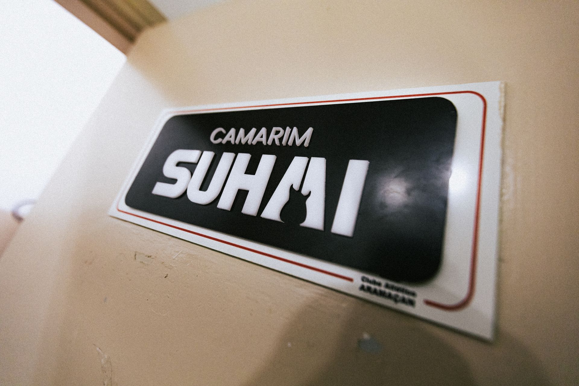 White nameplate reading “SUHAI” on a beige wall with a black center and red outline.