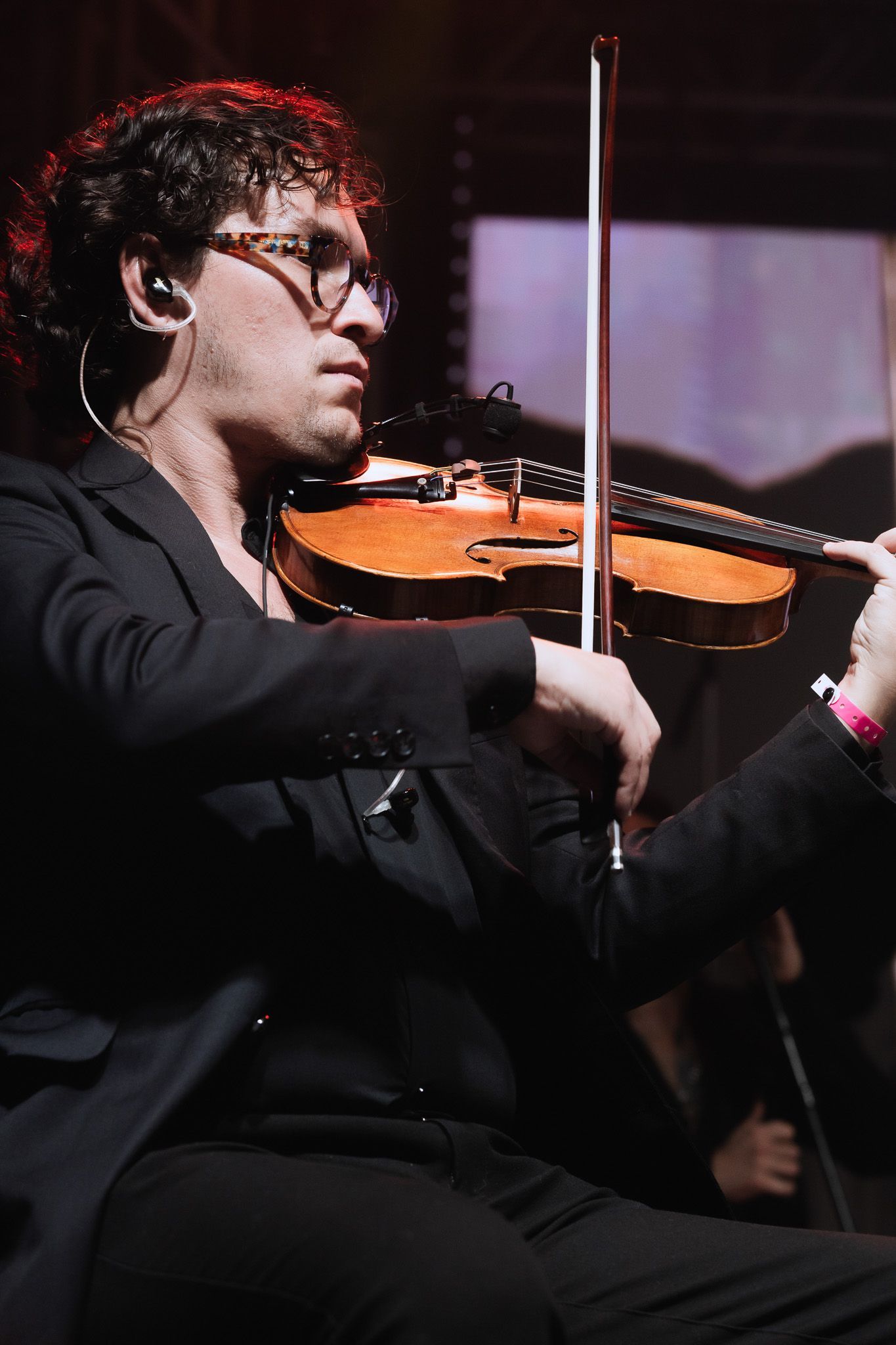 Violinista de terno preto tocando no palco sob uma iluminação aconchegante de concerto.