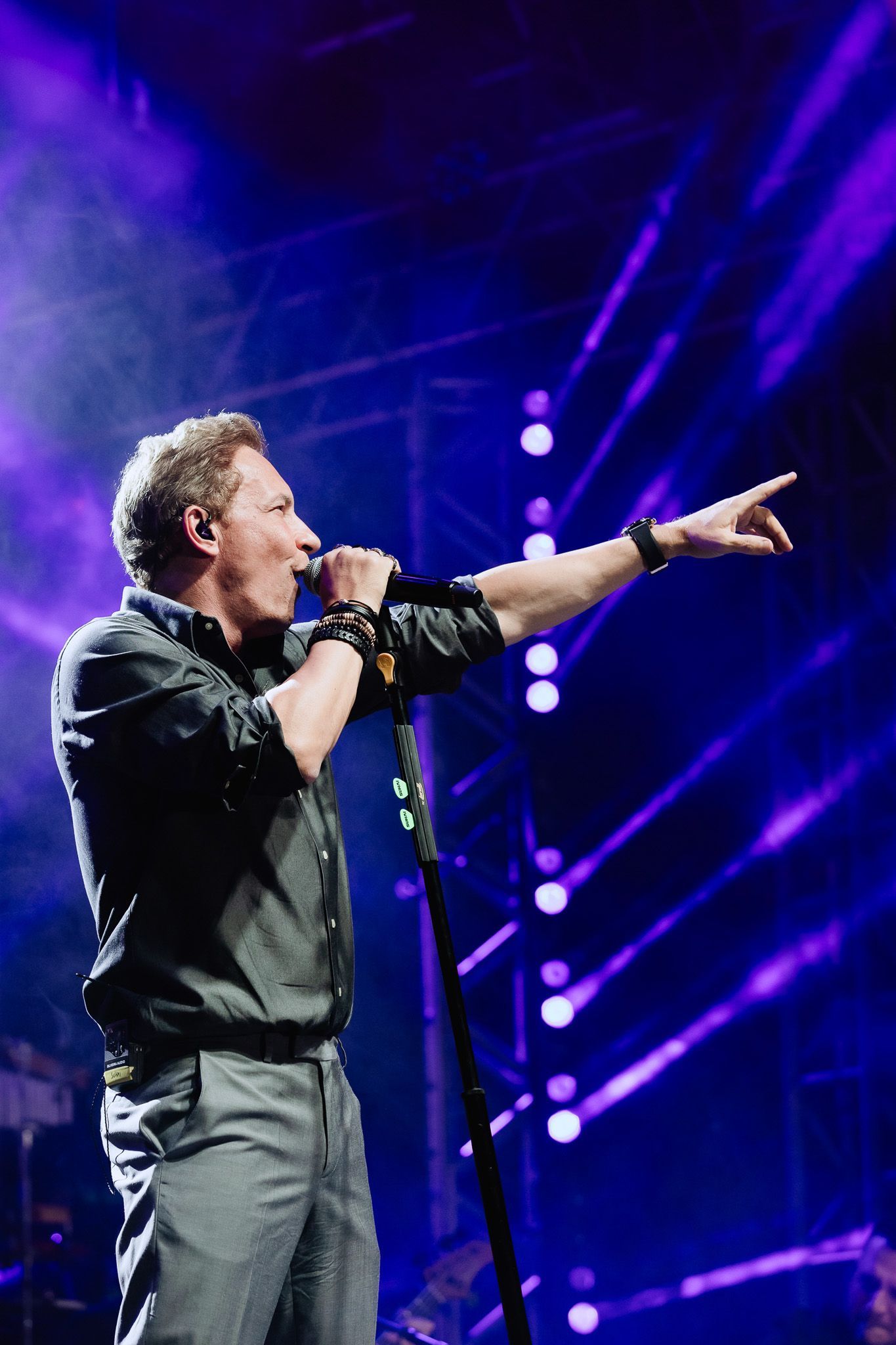 Cantor se apresentando no palco, apontando para a plateia sob luzes roxas de show.