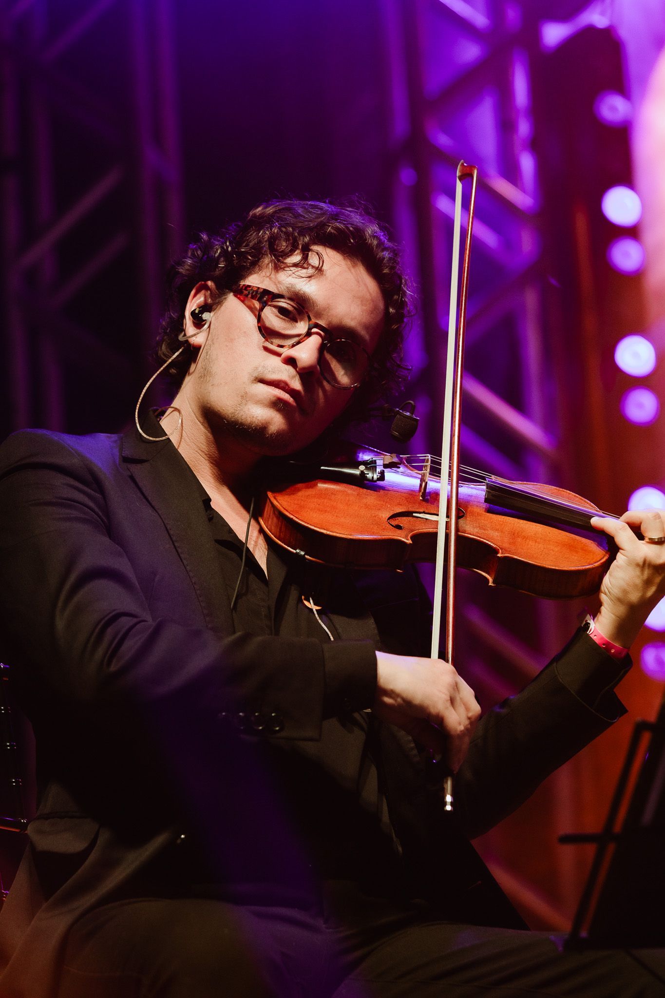 Músico tocando violino no palco sob iluminação roxa.