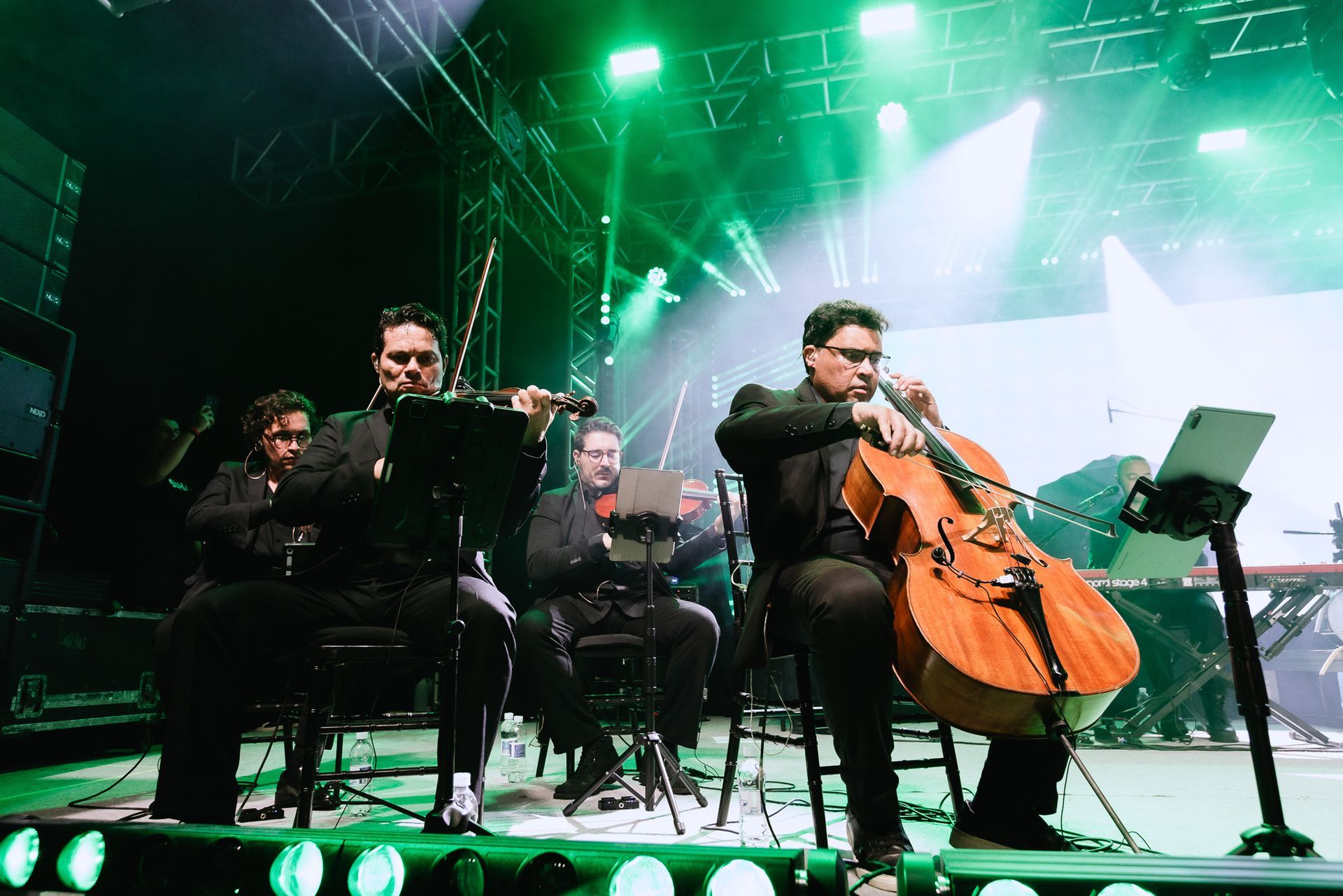Quarteto de cordas se apresentando no palco sob luzes verdes, com o violoncelo em primeiro plano.