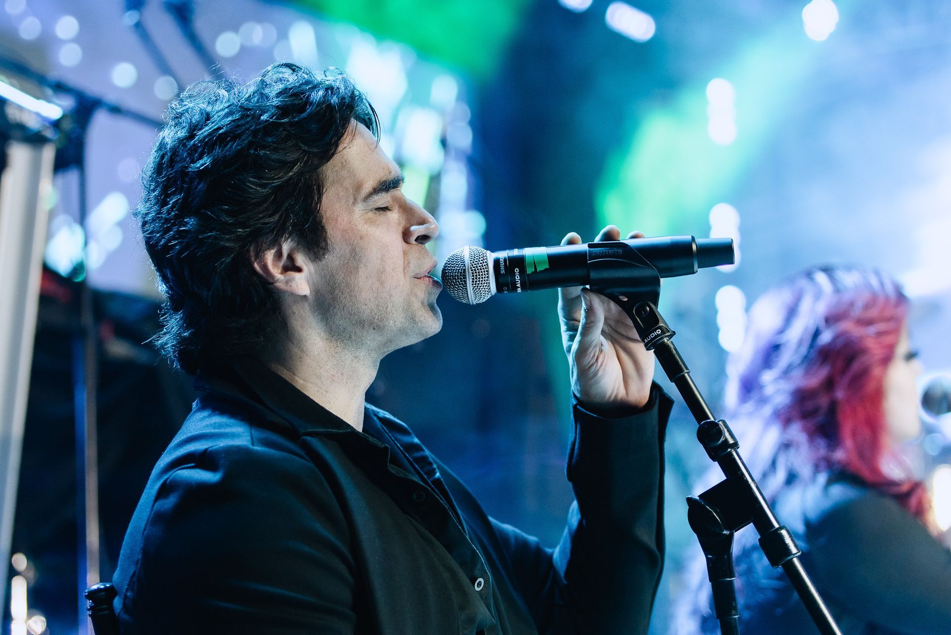 Cantor se apresentando ao microfone em um palco iluminado por luz azul.