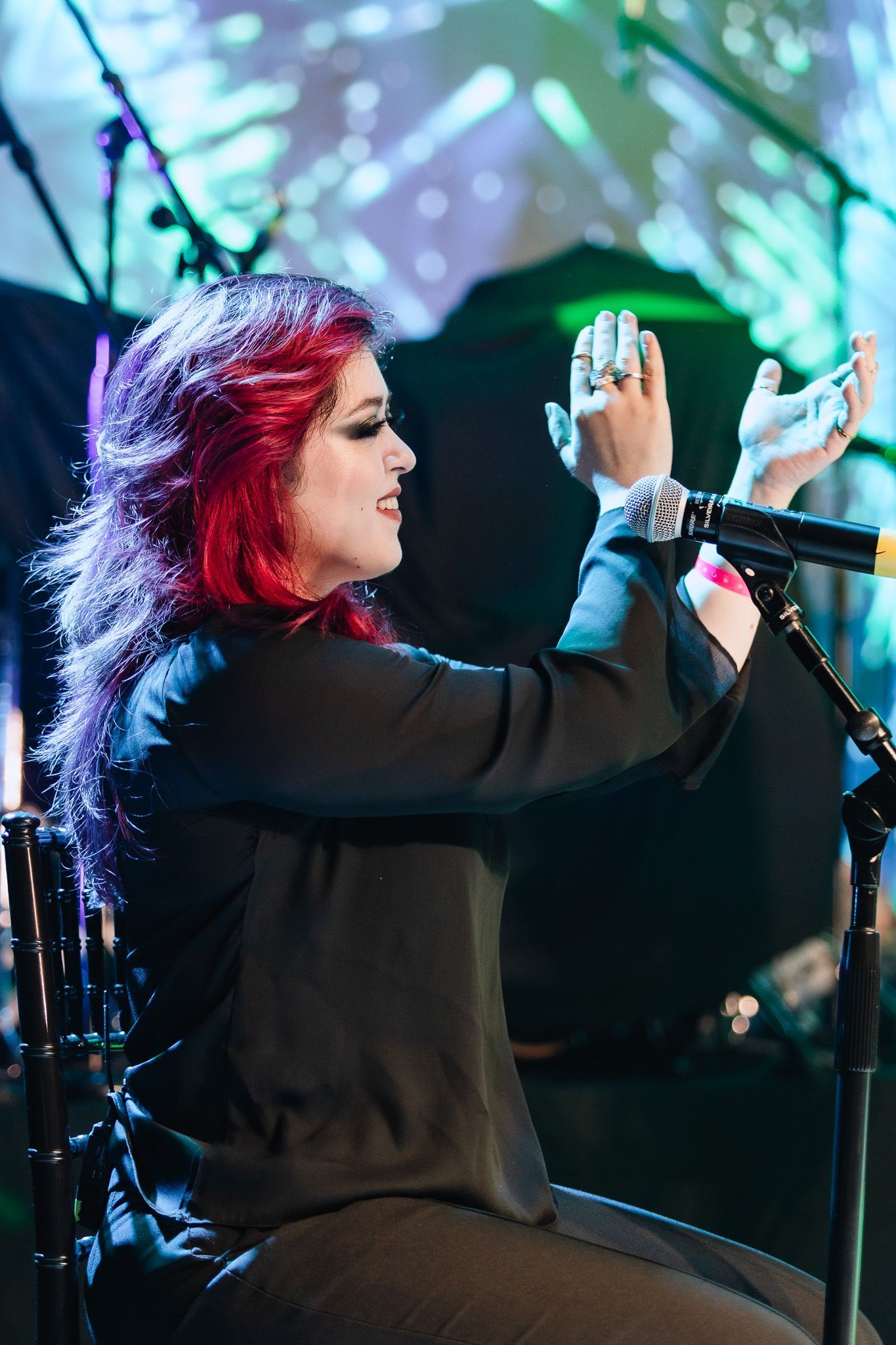 Cantor ruiva batendo palmas no palco ao lado de um microfone, sob luzes coloridas de um show.