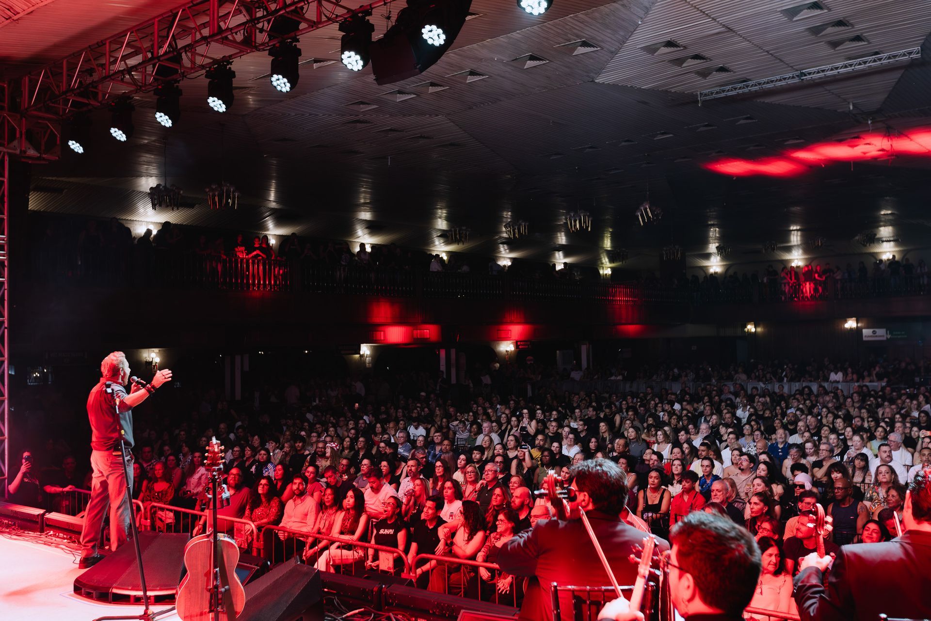 Palestrante discursando para uma grande plateia em um auditório iluminado em vermelho.