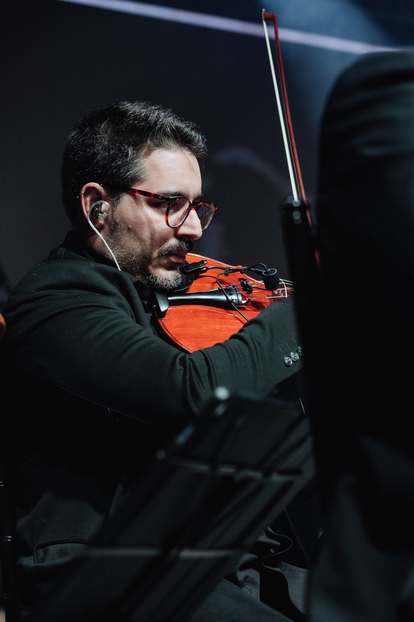 Músico tocando um violino vermelho em um palco com pouca luz.