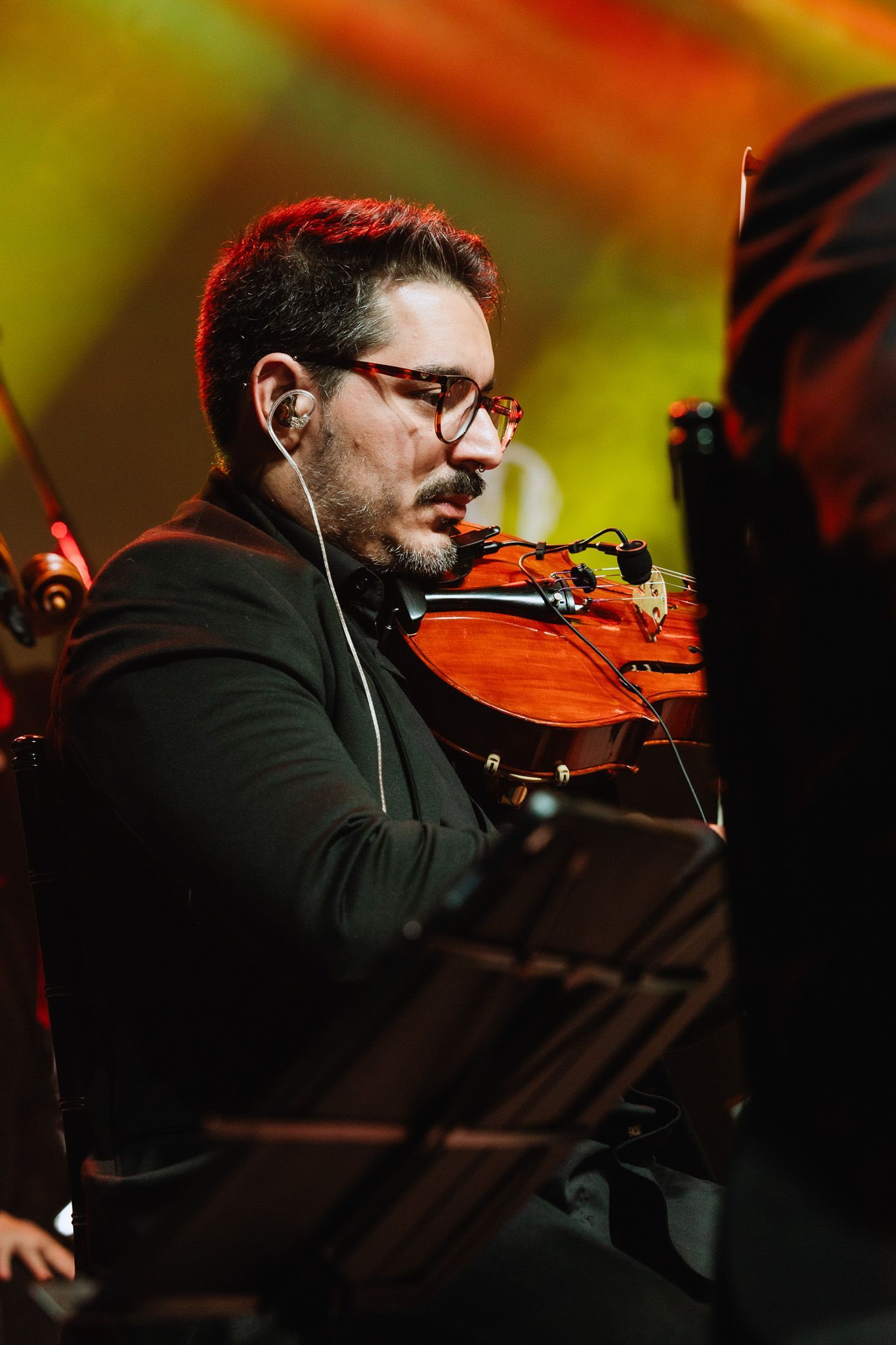 Homem tocando violino no palco sob iluminação laranja quente