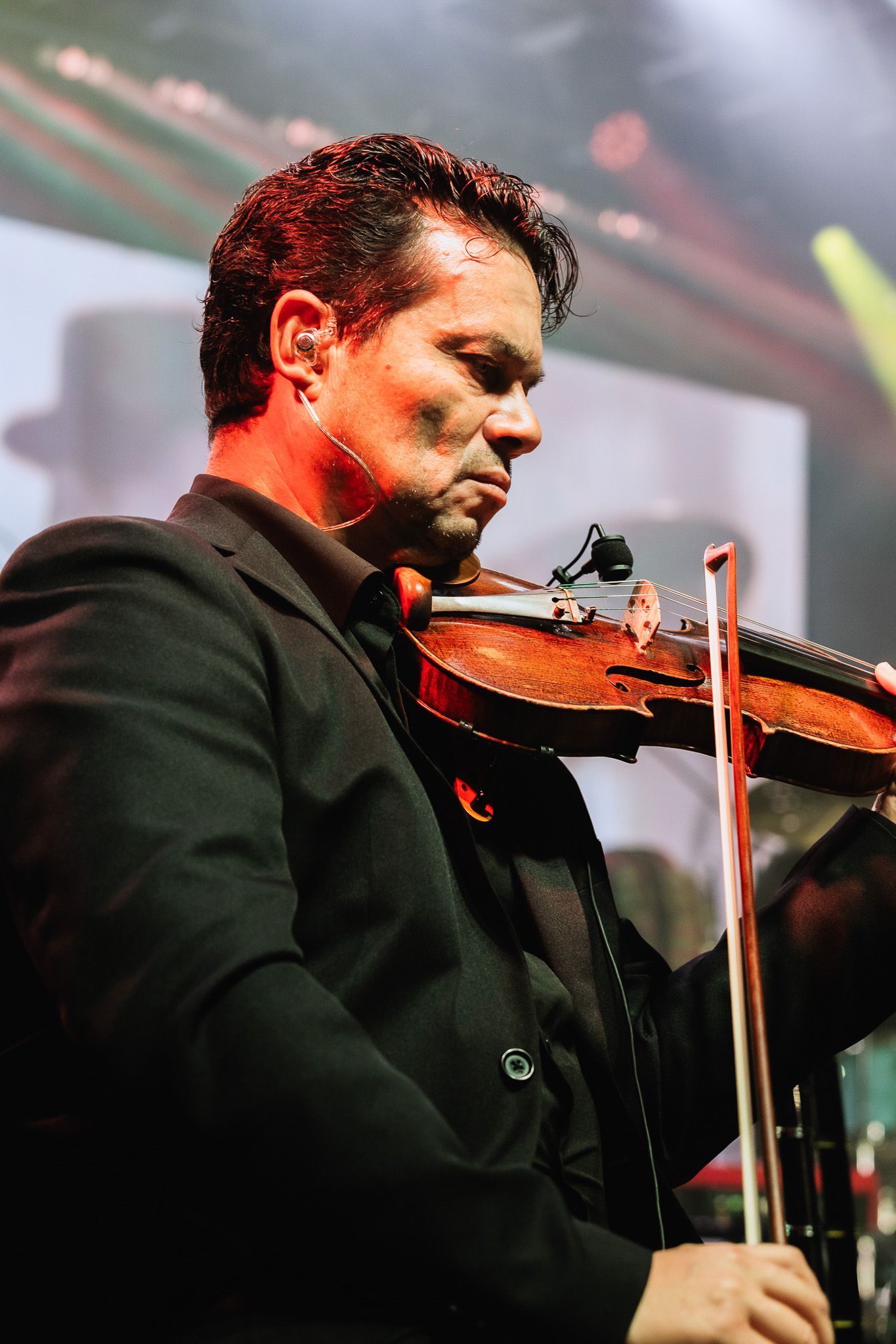 Músico tocando violino no palco sob luzes vermelhas e verdes.