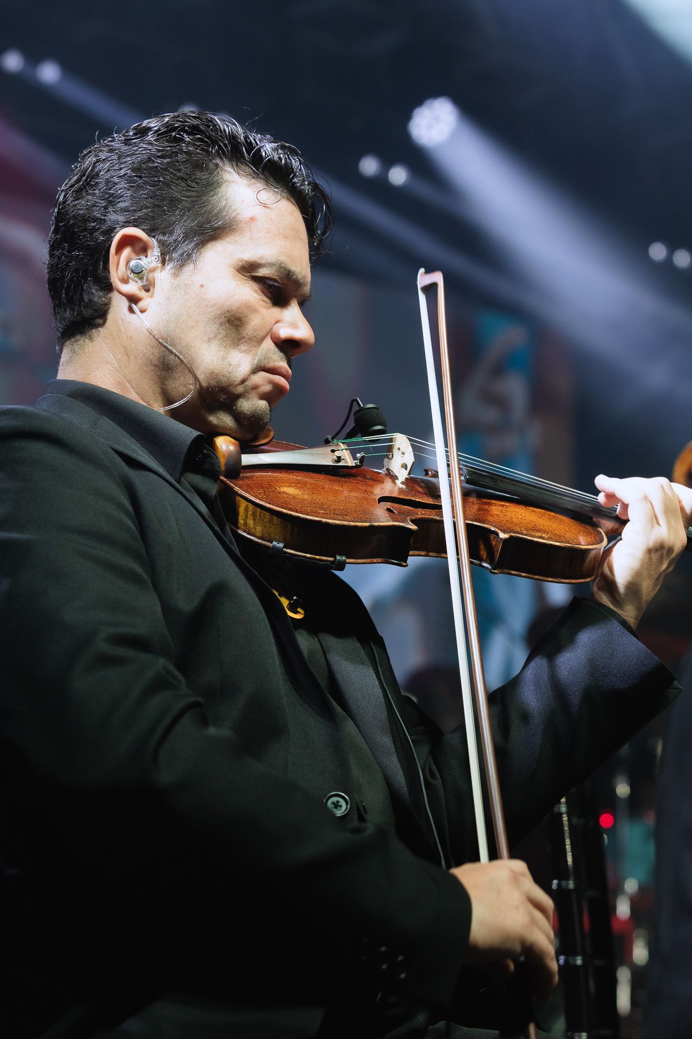 Violinista de terno escuro tocando no palco sob luzes brilhantes de concerto.