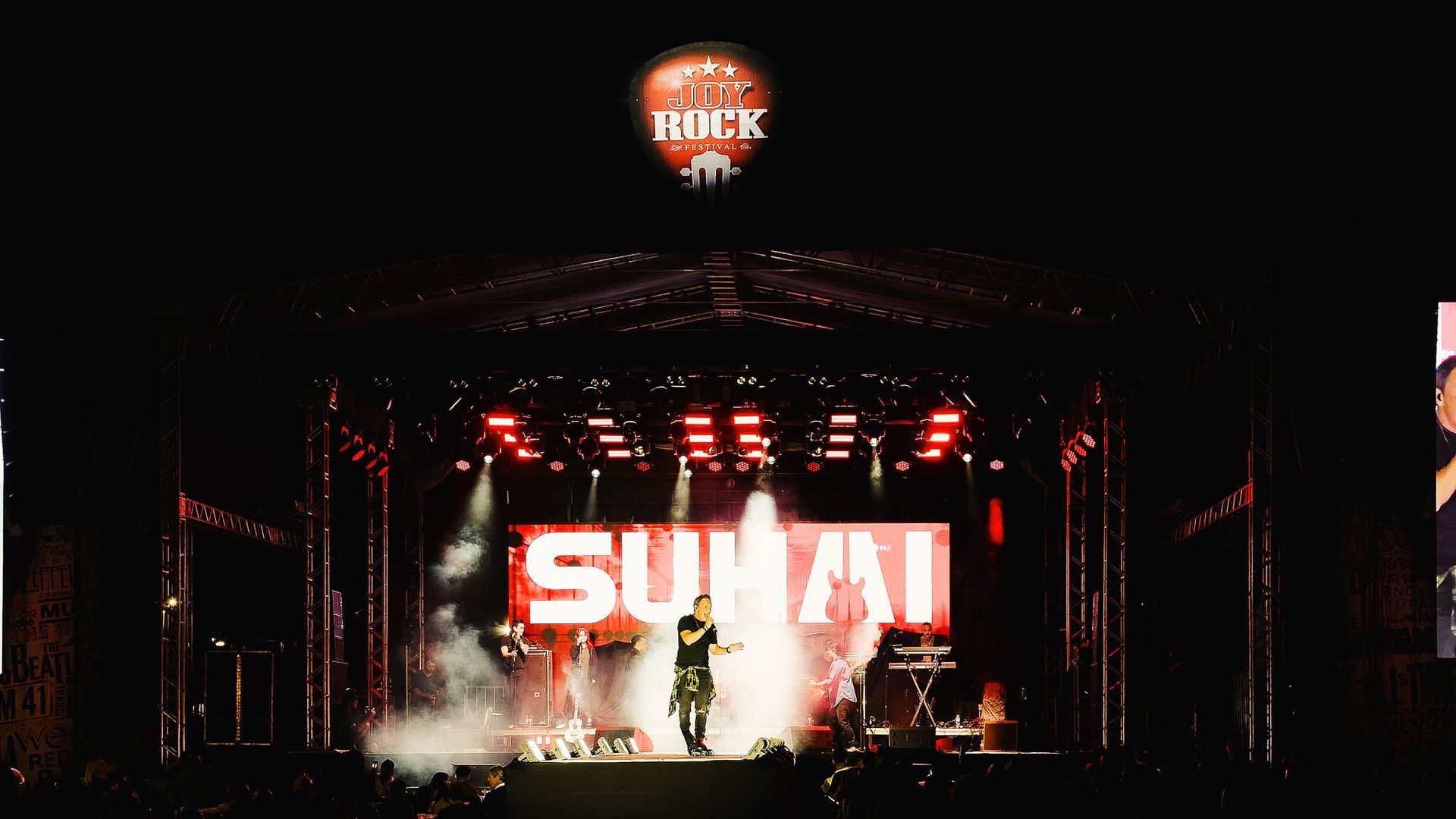 Palco de concertos com luzes vermelhas brilhantes e um grande telão com a inscrição “SUHAI” à noite.