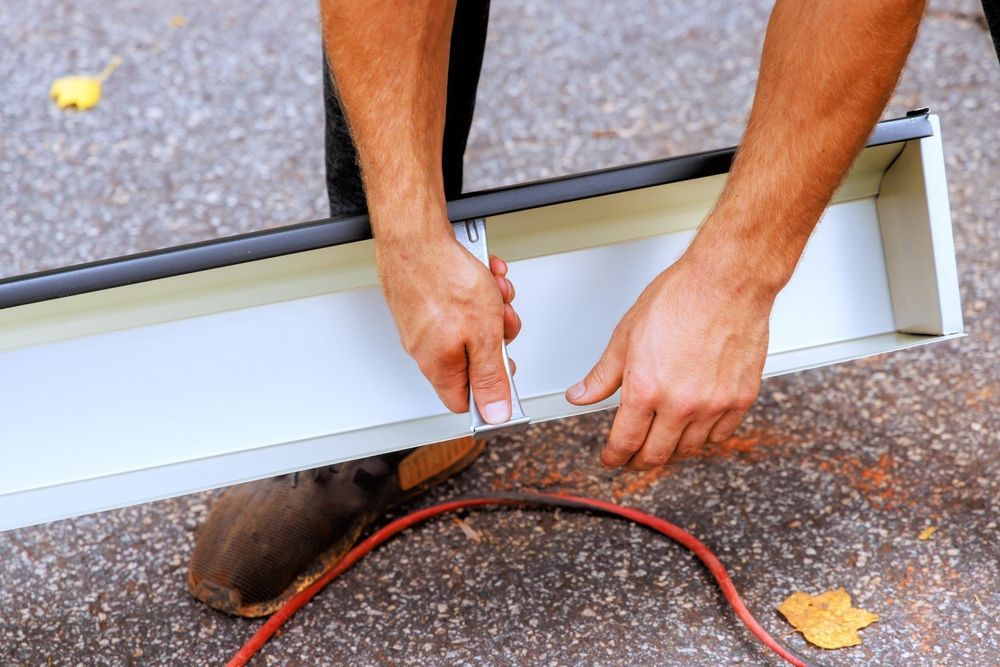 Person using a tool to work on a white metal gutter on an outdoor surface.