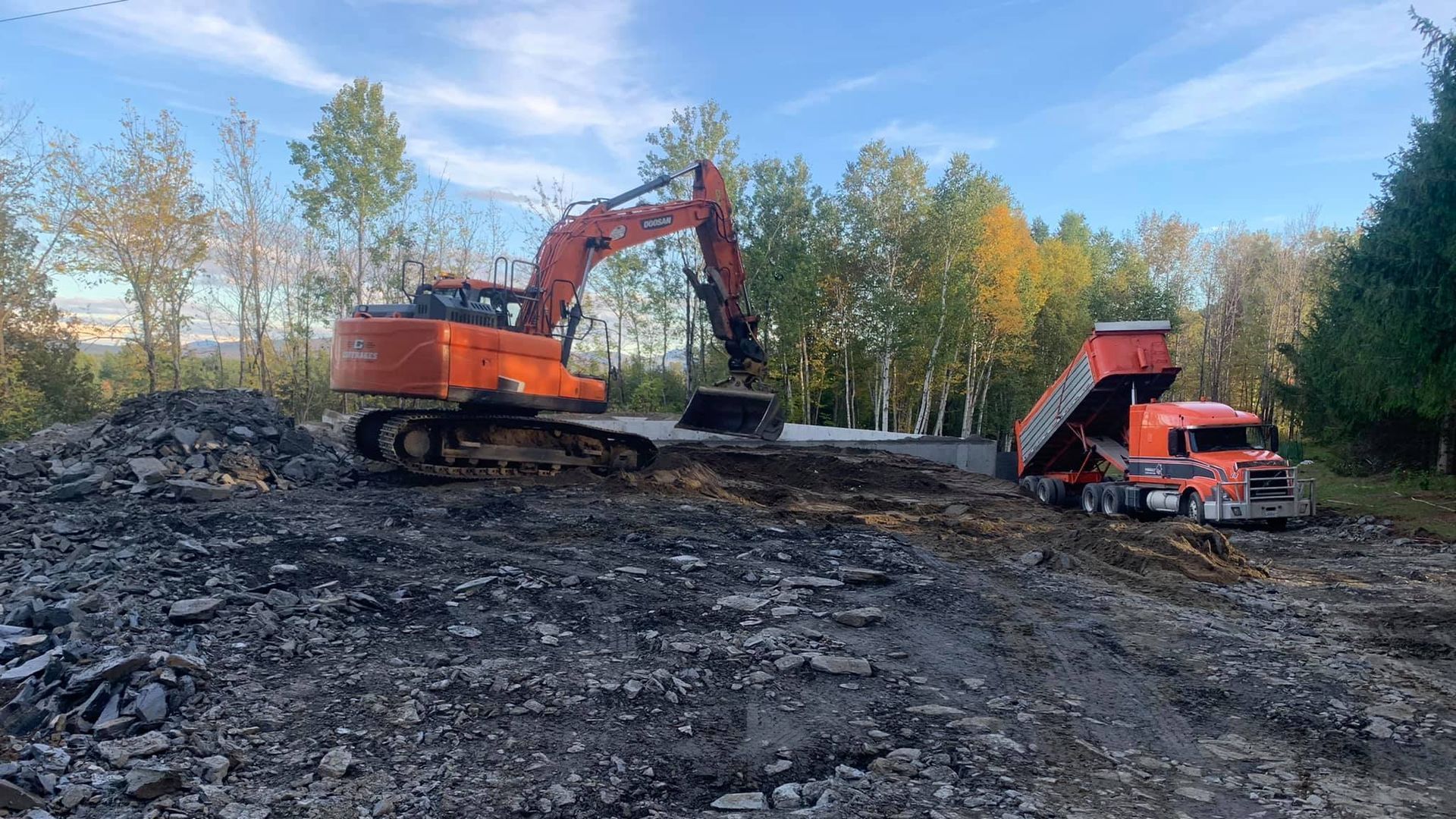 Une excavatrice chargeant un camion à benne basculante avec des débris sombres à l'extérieur sur un chantier de construction.