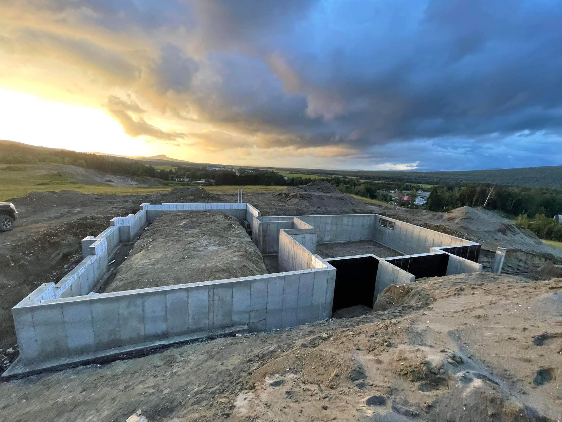 Fondation en béton pour un bâtiment en construction sur une colline, ciel nuageux.