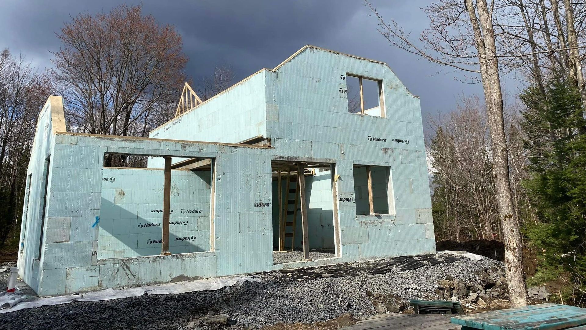 Maison en béton bleu isolée en construction, extérieur, bois, ciel couvert.