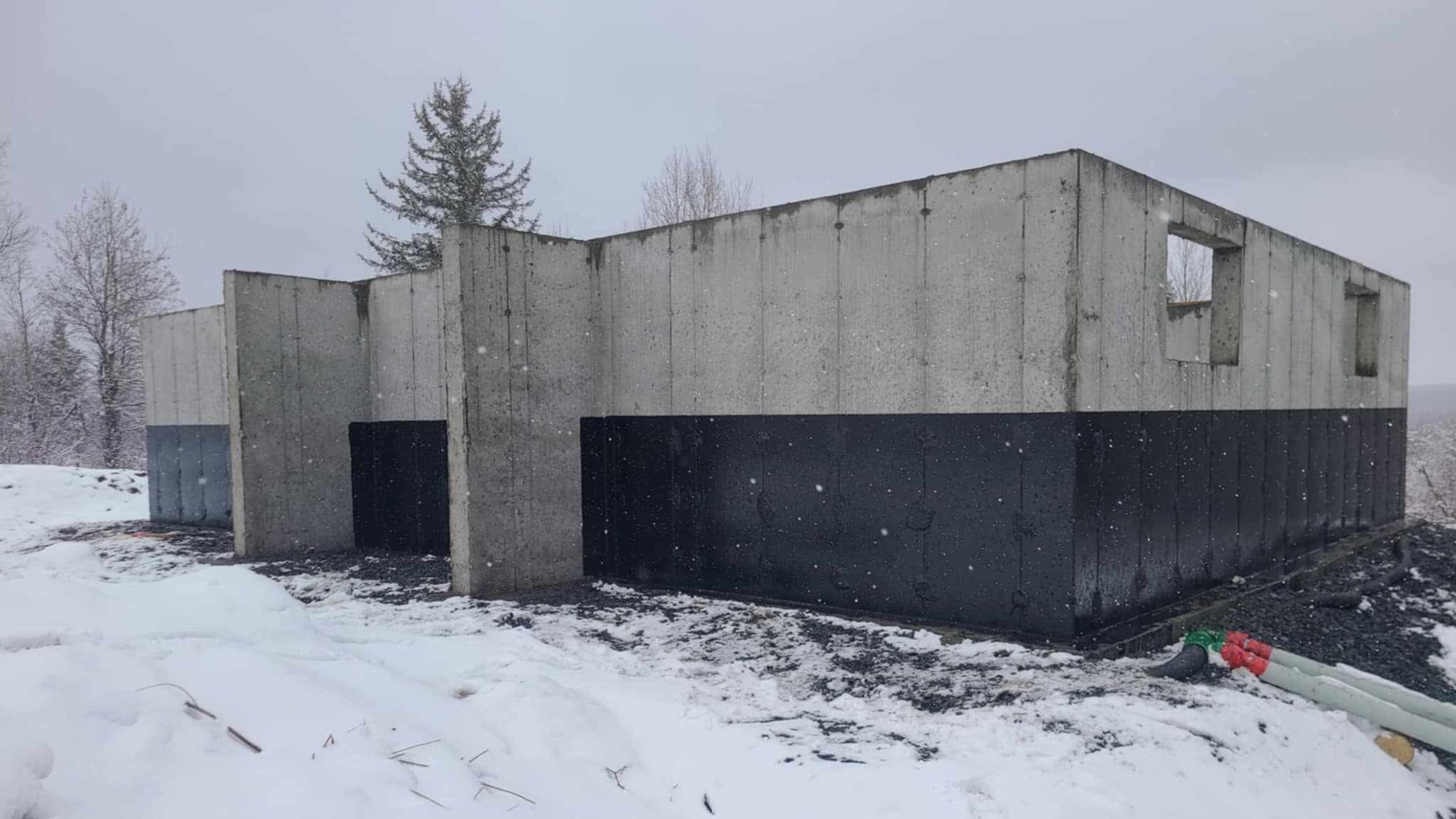 Fondation en béton d'un bâtiment en construction dans un environnement enneigé.