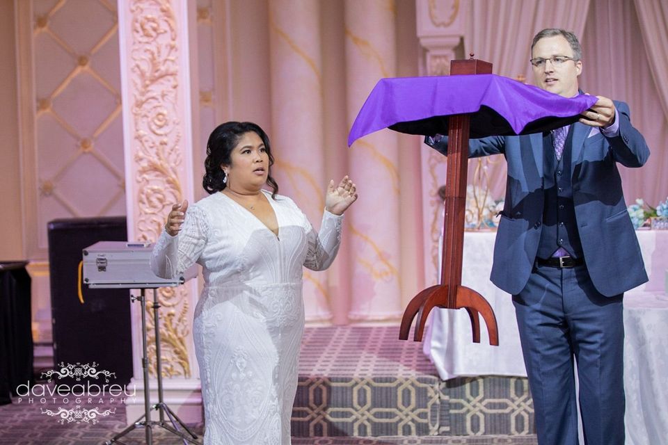 A man in a suit and a woman in a white dress are performing a magic trick.