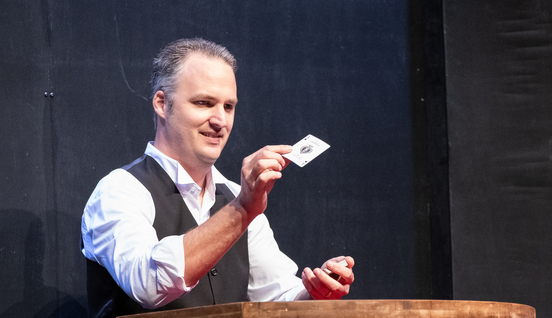 A man in a white shirt and black vest is holding a card in his hand.