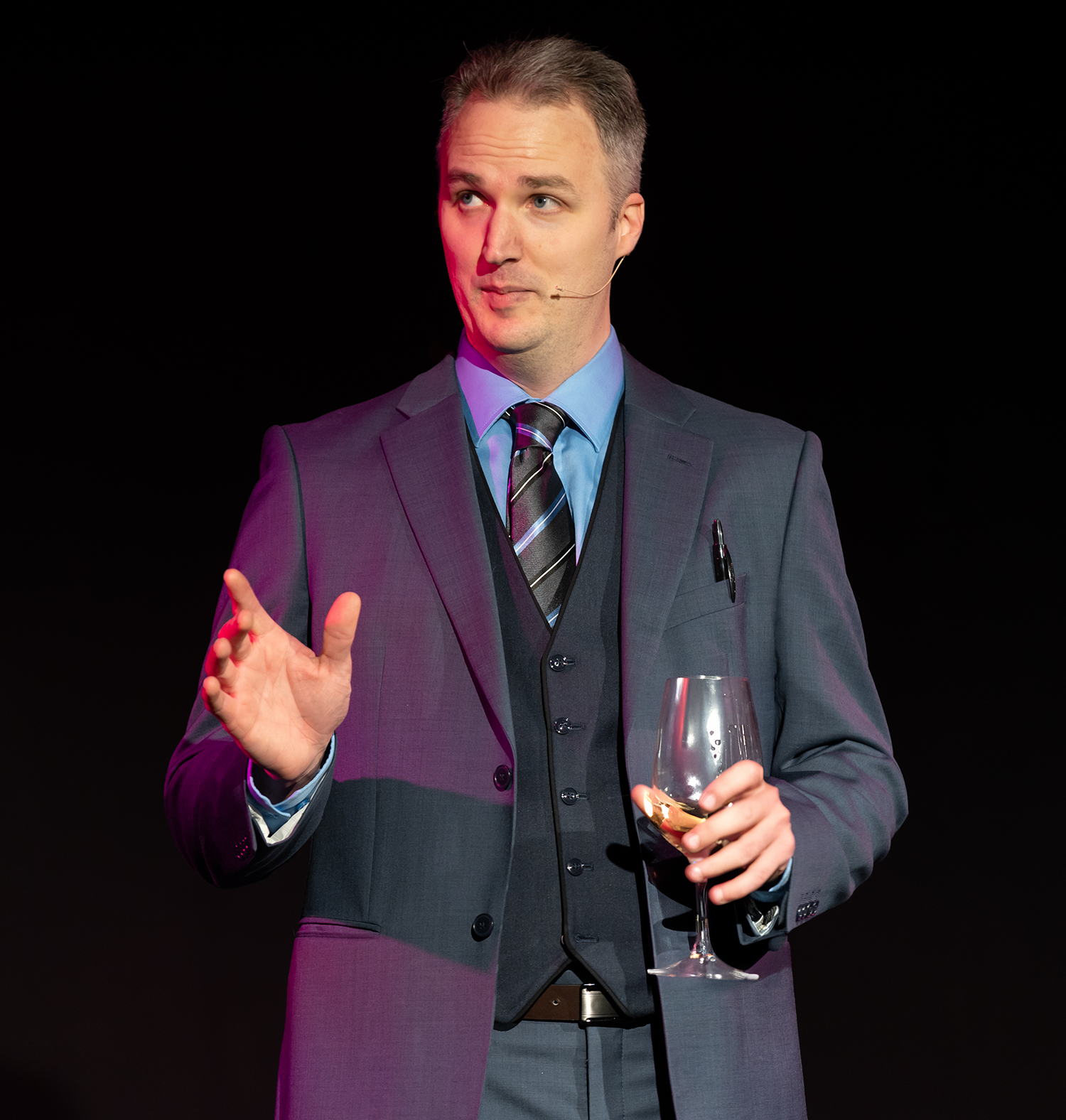A man in a suit and tie is holding a glass of wine.