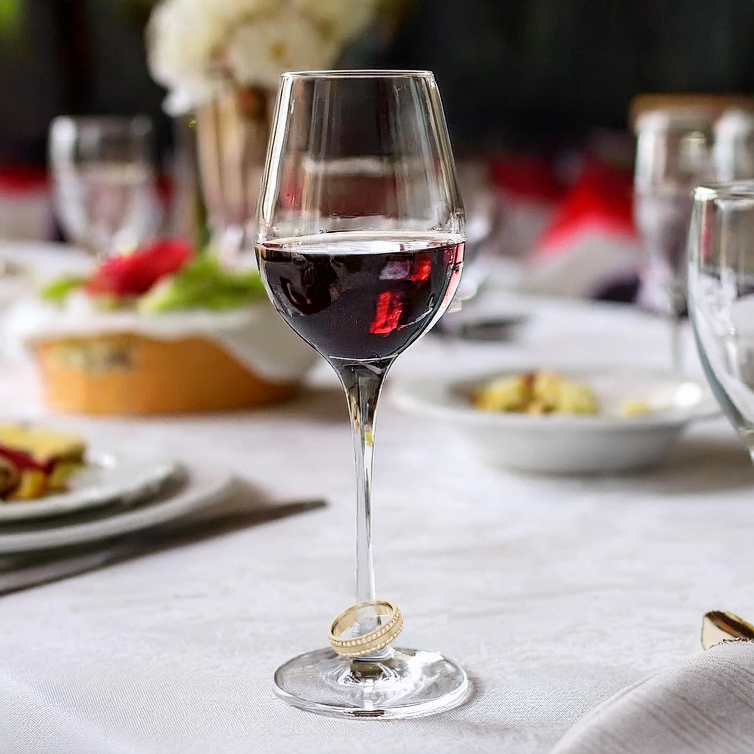 A glass of wine with a wedding ring on it is on a table.