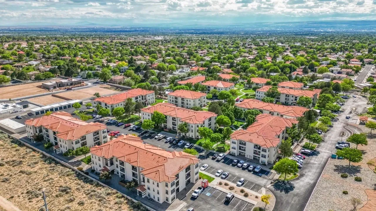 Aerial view of apartment buildings with red tile roofs surrounded by trees and parking lots at La Ventana, offering apartments in Albuquerque, NM.