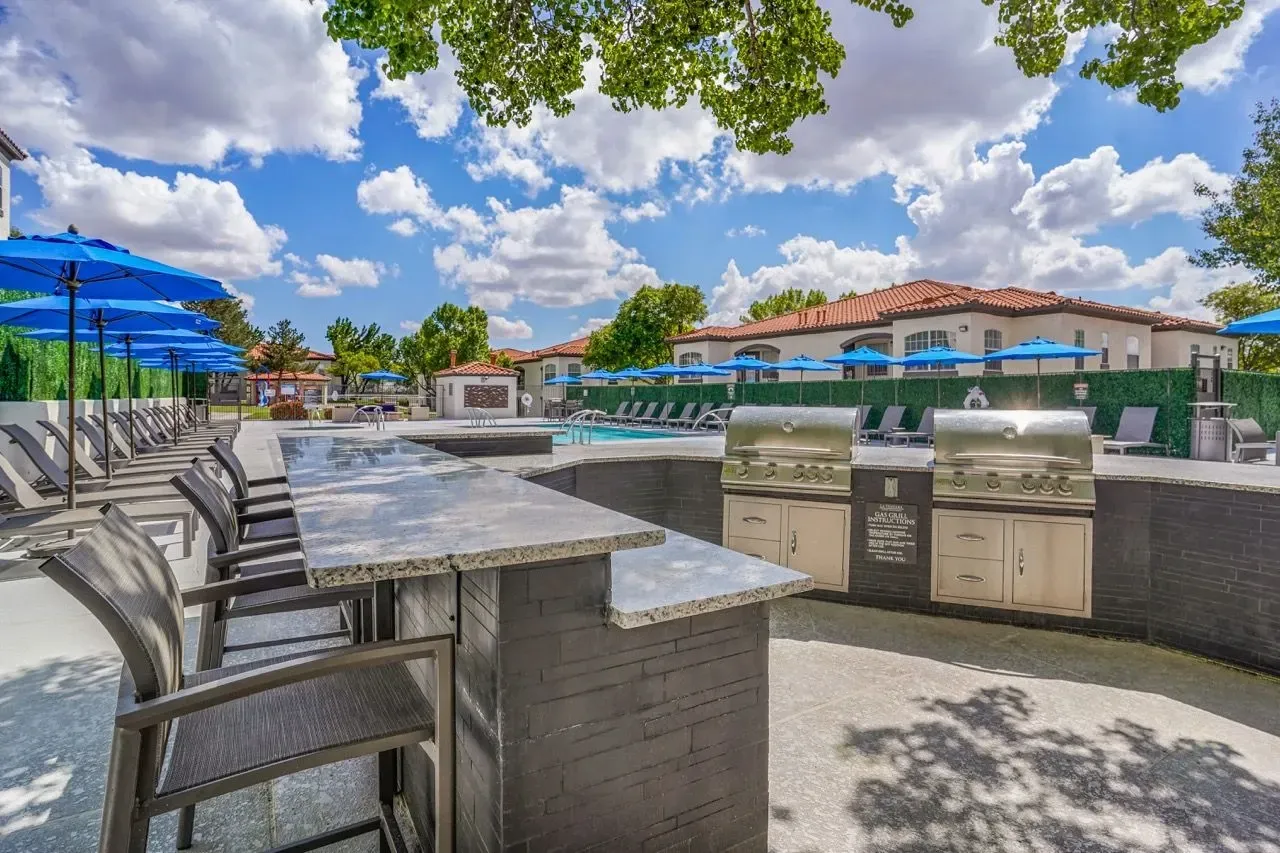 Outdoor grilling station with two stainless steel grills and a granite countertop bar, adjacent to a swimming pool and lounge chairs at La Ventana, offering apartments in Albuquerque, NM.