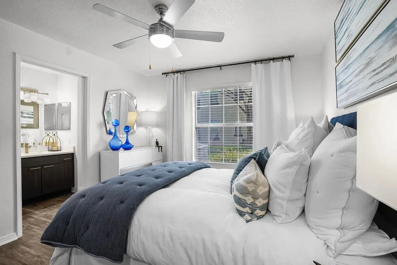 Luxurious bedroom with a king-size bed, white linens, and blue accent pillows, leading into an ensuite bathroom at La Ventana, offering apartments in Albuquerque, NM.