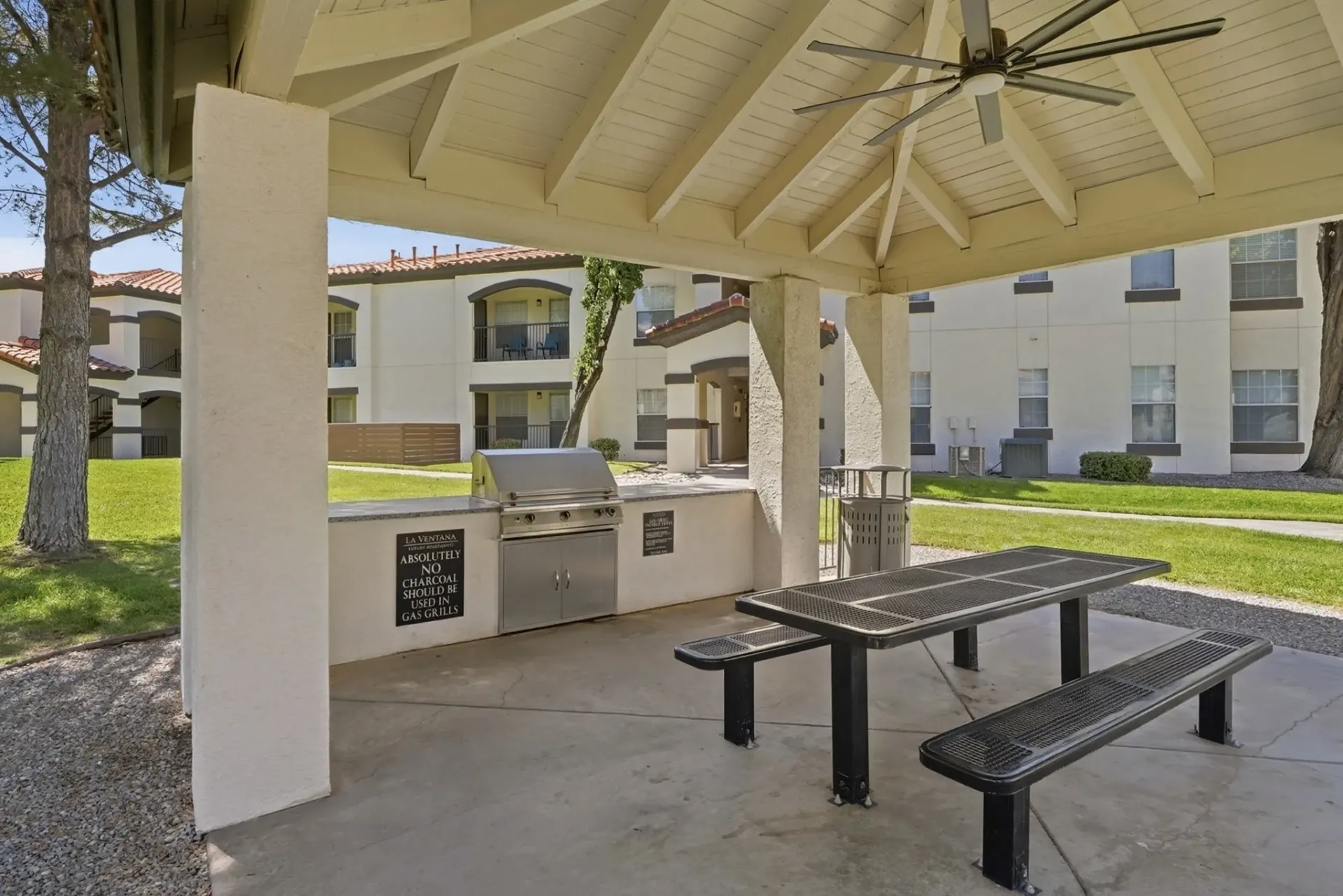 Outdoor grilling station with a built-in gas grill and picnic table under a covered pavilion at La Ventana, offering apartments in Albuquerque, NM.
