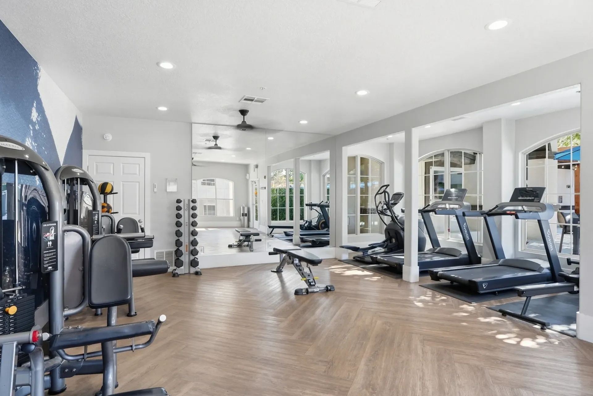 Treadmills and elliptical machines in a well-lit gym with mirrors and wood floors at La Ventana, offering apartments in Albuquerque, NM.