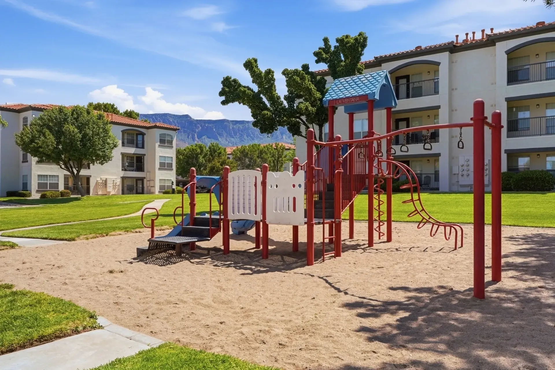 Playground equipment with apartment buildings in the background at La Ventana, offering apartments in Albuquerque, NM.