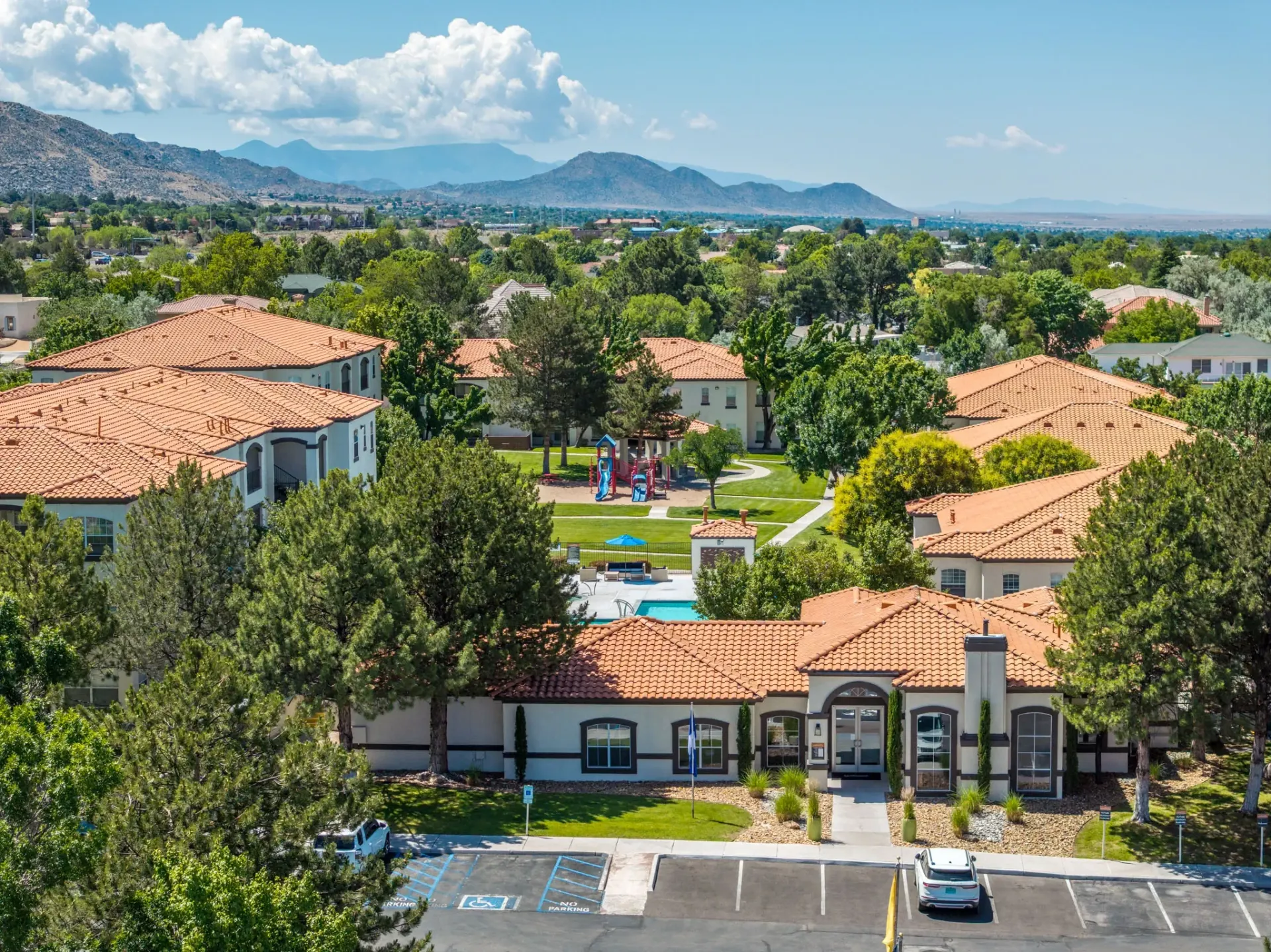 Aerial view of apartment complex with pool, playground, and mountain backdrop at La Ventana, offering apartments in Albuquerque, NM.