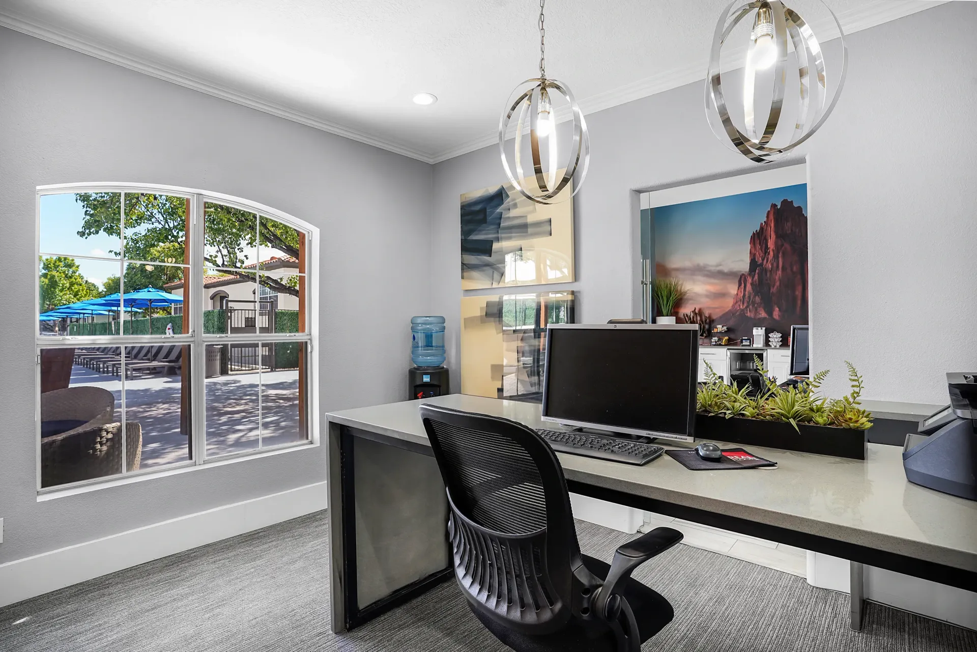 Modern home office with desk, computer, chair, wall art, and large window view at La Ventana, offering apartments in Albuquerque, NM.