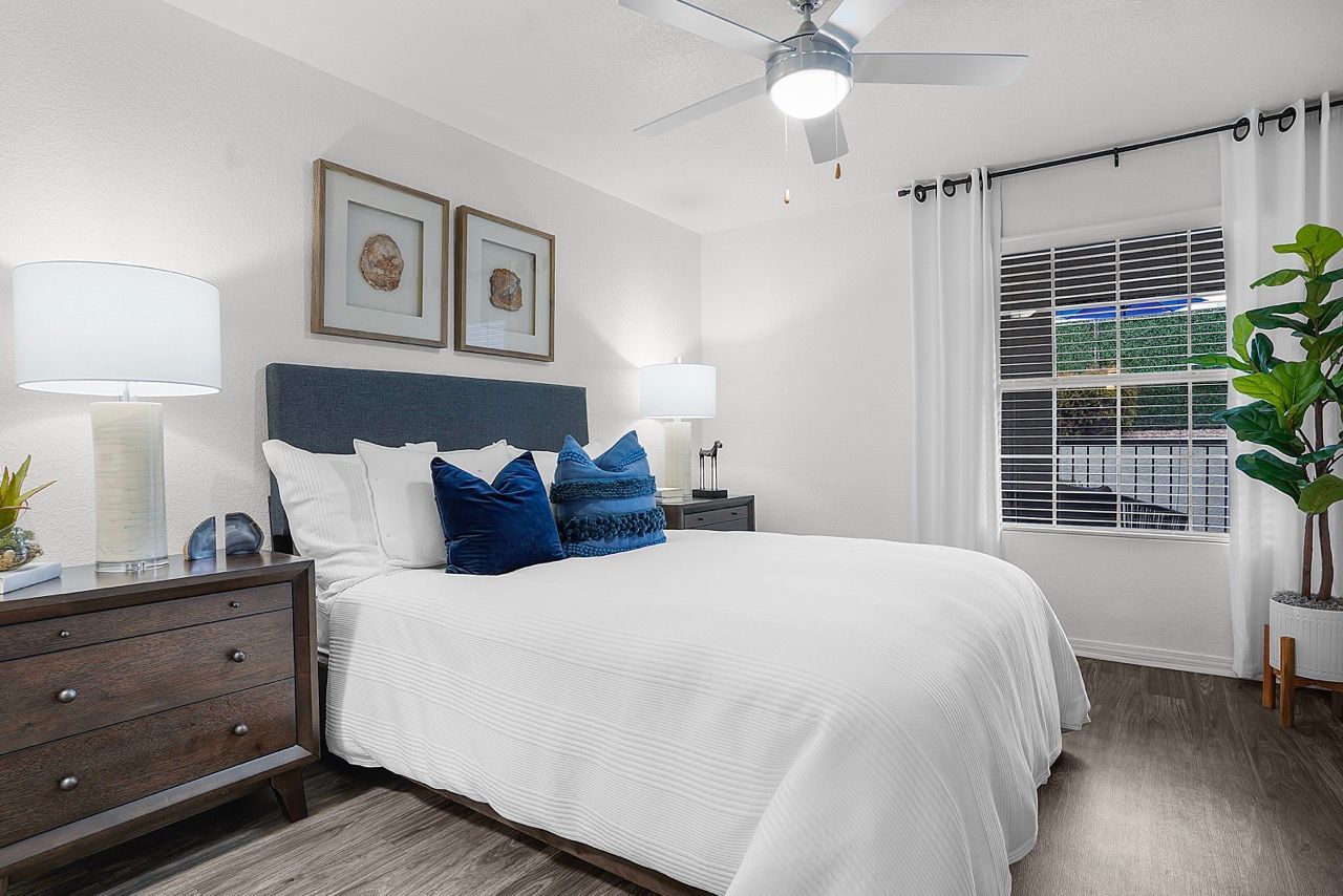 Bedroom with queen bed, two dark wood nightstands, ceiling fan, and a large window with white curtains.