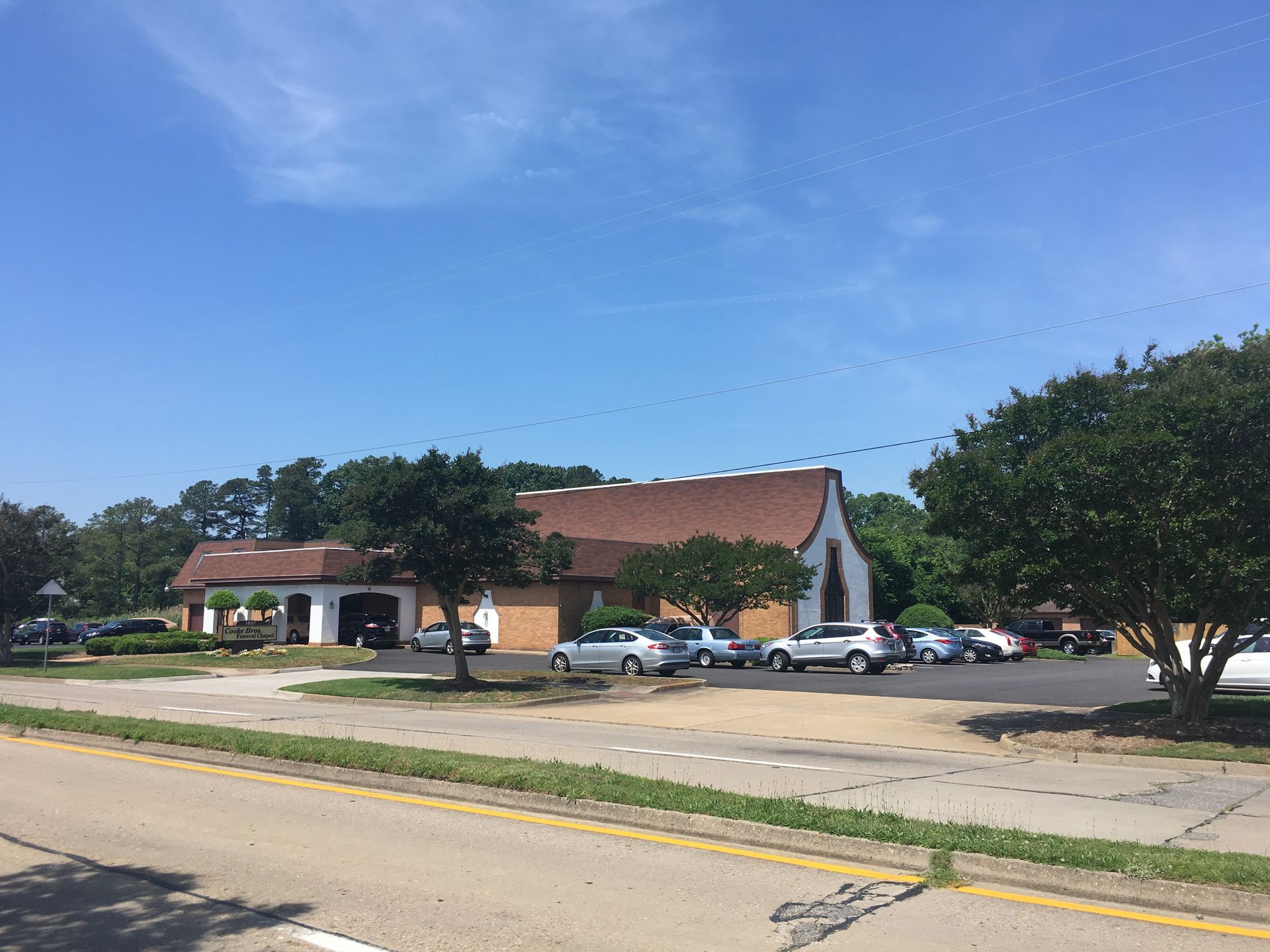 A brown, roofed commercial building with a parking lot and trees under a clear blue sky.