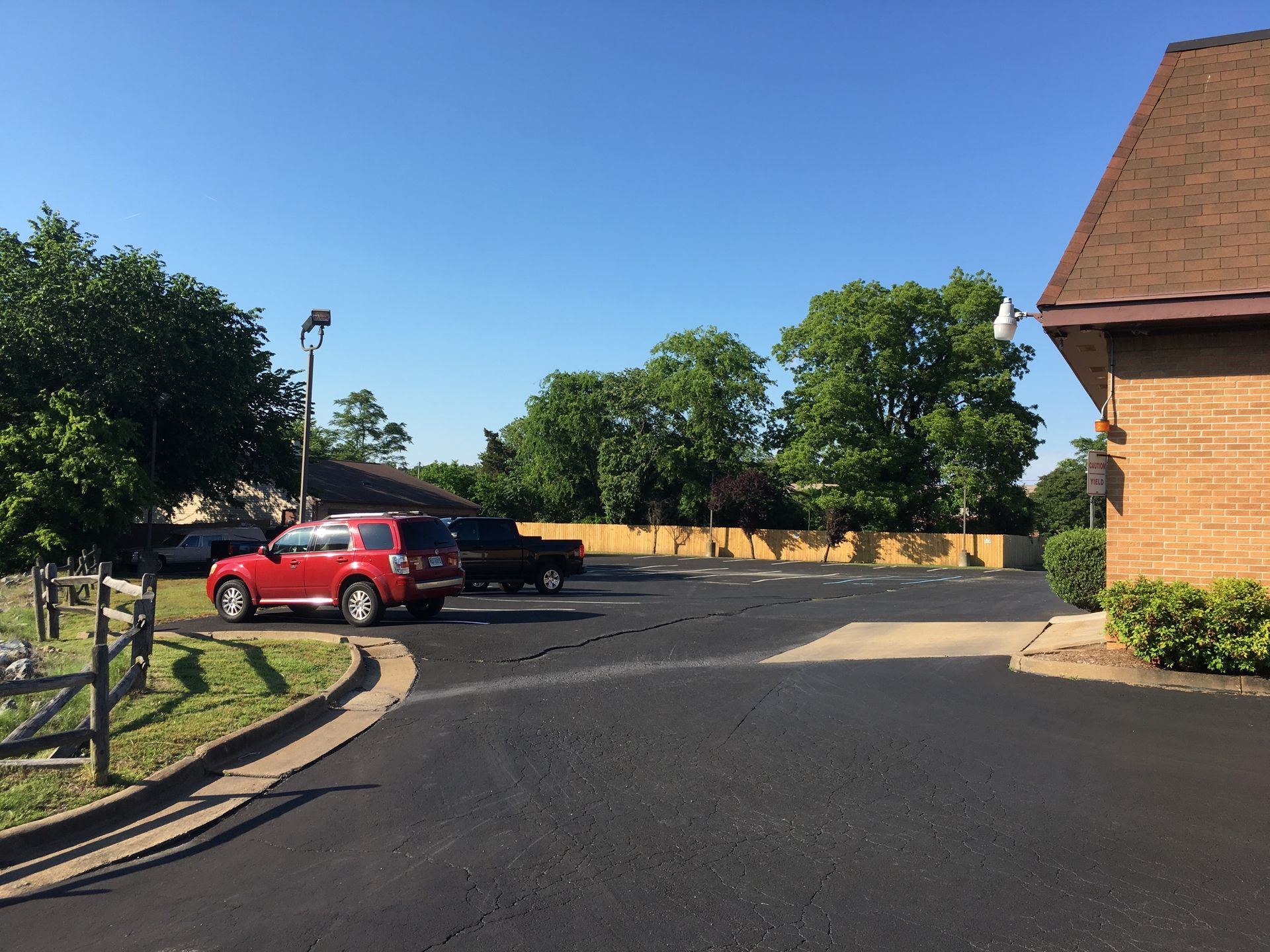 A parking lot with a red SUV, a black pickup truck, and a brick building under a clear blue sky.
