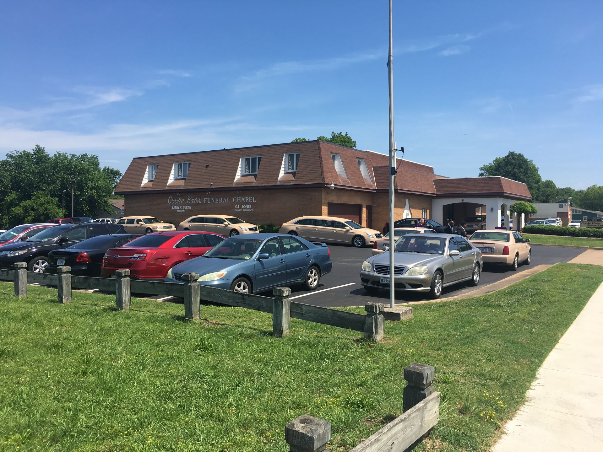 A brown building with a mansard roof and a parking lot with several cars under a clear blue sky.