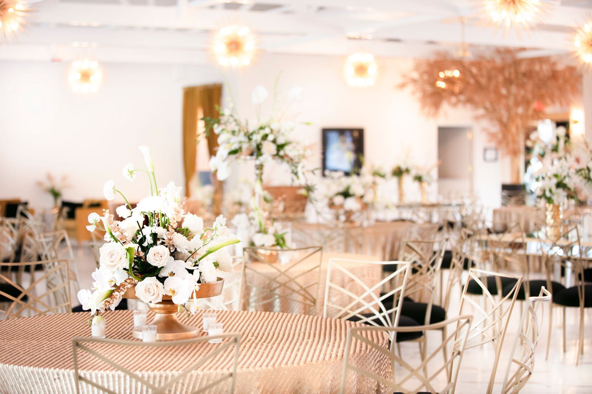 Elegant wedding reception room with gold sequined tablecloths, white floral centerpieces, and decorative light fixtures.