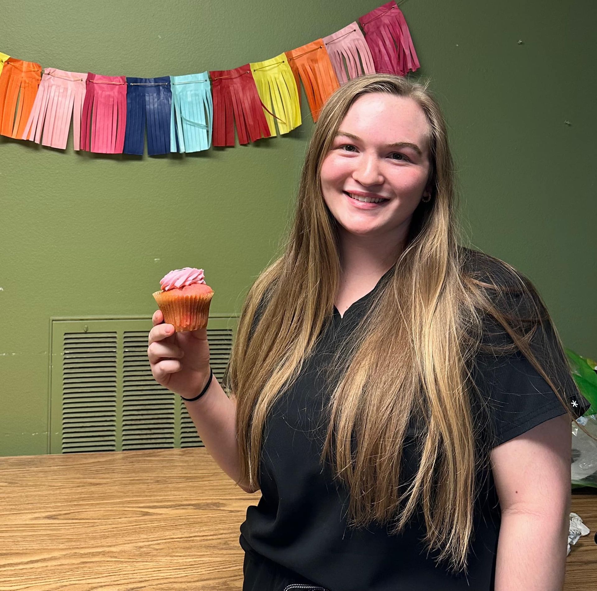 A woman in a black shirt is holding a pink cupcake