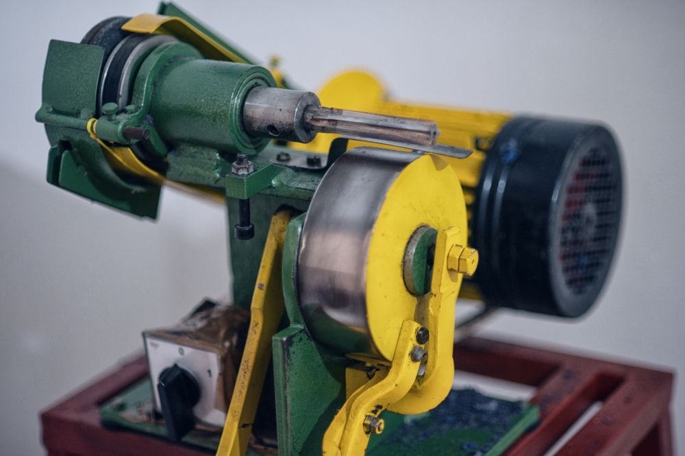Green and yellow industrial grinding machine on a wooden base, used for sharpening.