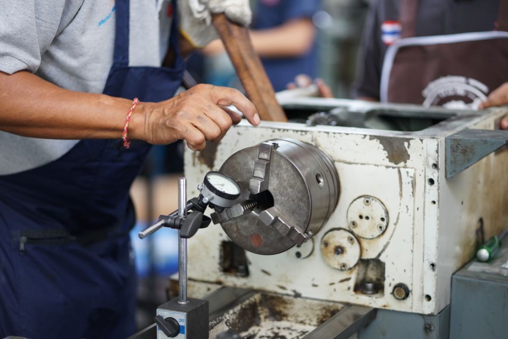 Man using a dial indicator on a lathe chuck; workshop setting.