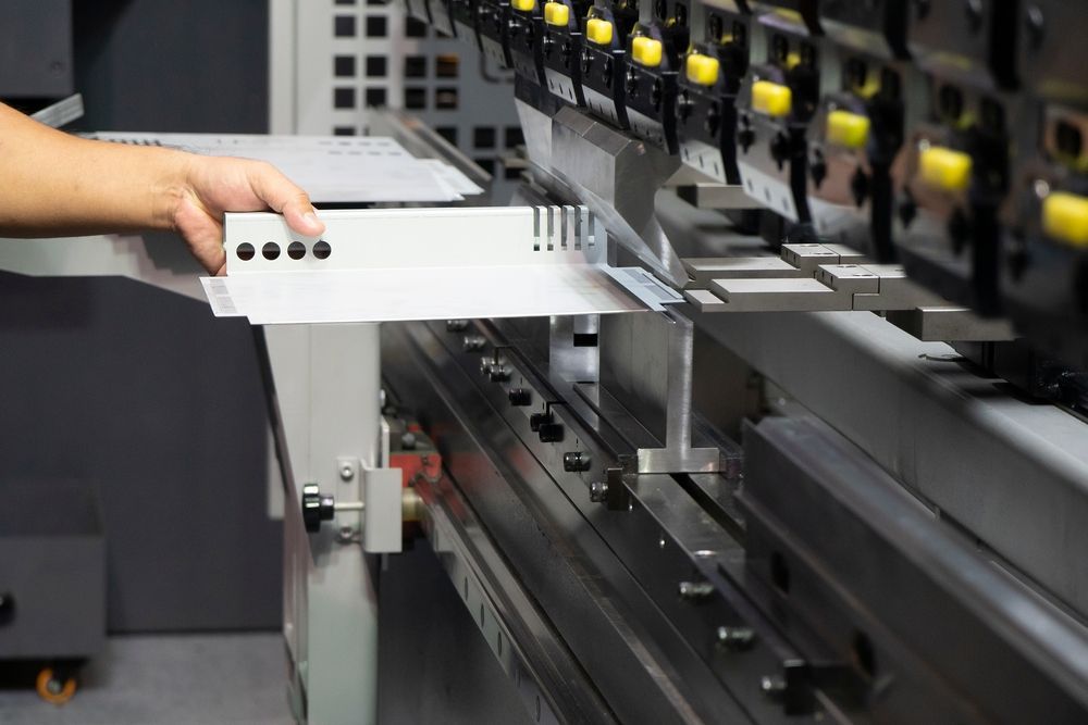 Person bending metal sheet with industrial machine.