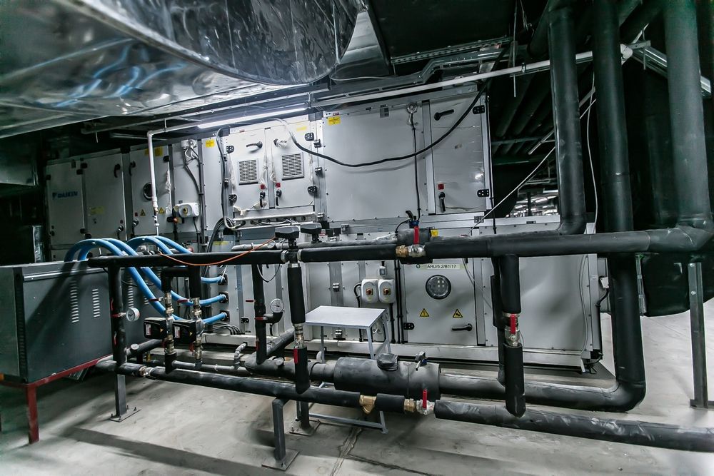 HVAC system in a room with pipes and ducts, mostly gray with black insulated pipes and some blue.