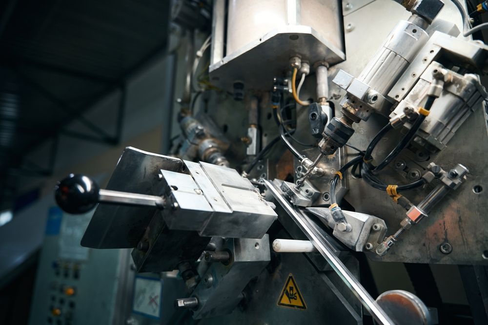 Industrial machine close-up, working on a metal rod, with various mechanical parts and warning labels.