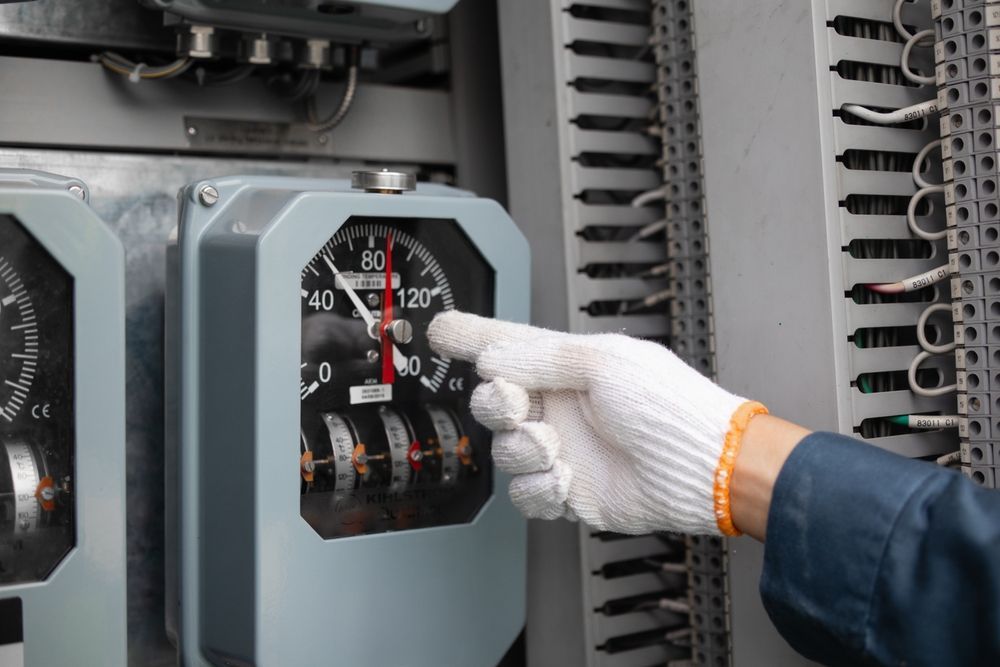 Hand in a white glove adjusting a gauge on an industrial control panel.