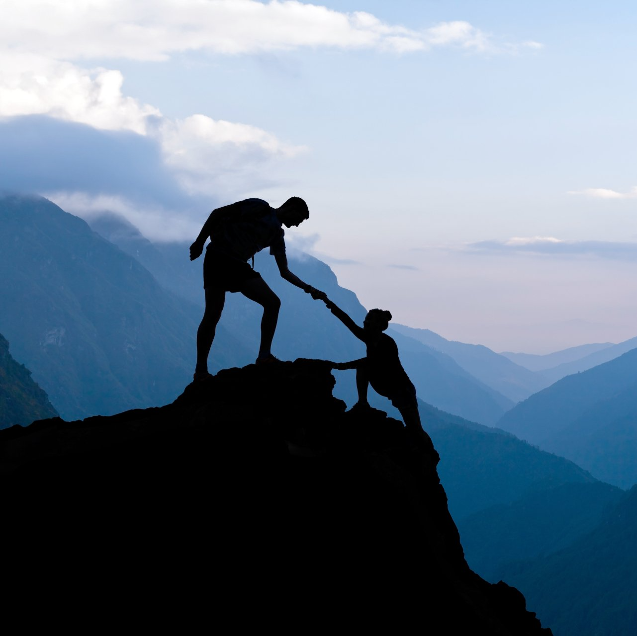 A silhouette of a man helping a woman climb a mountain