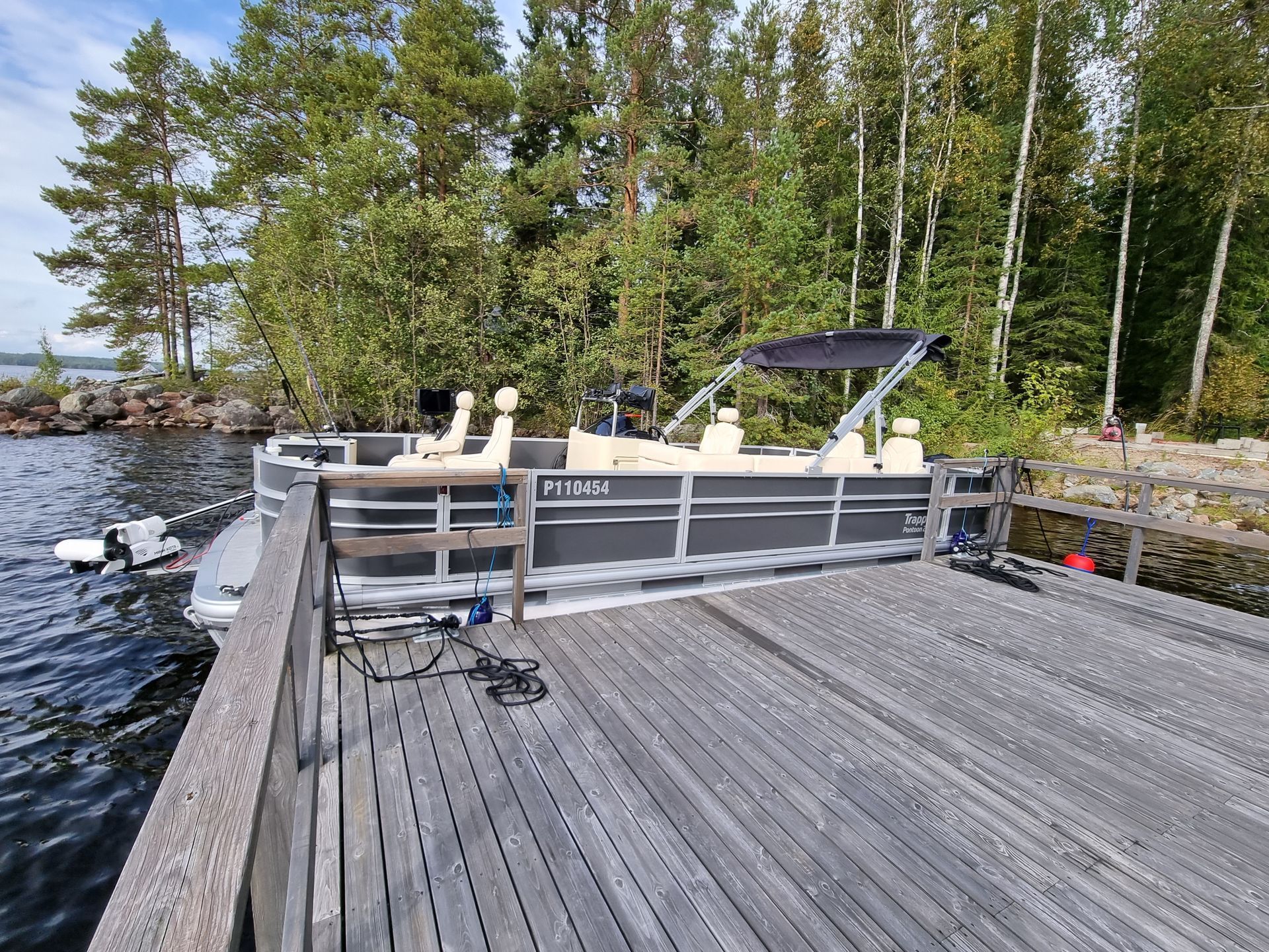 Wooden dock with fishing barge beside a calm lakeshore and pine trees under a clear sky
