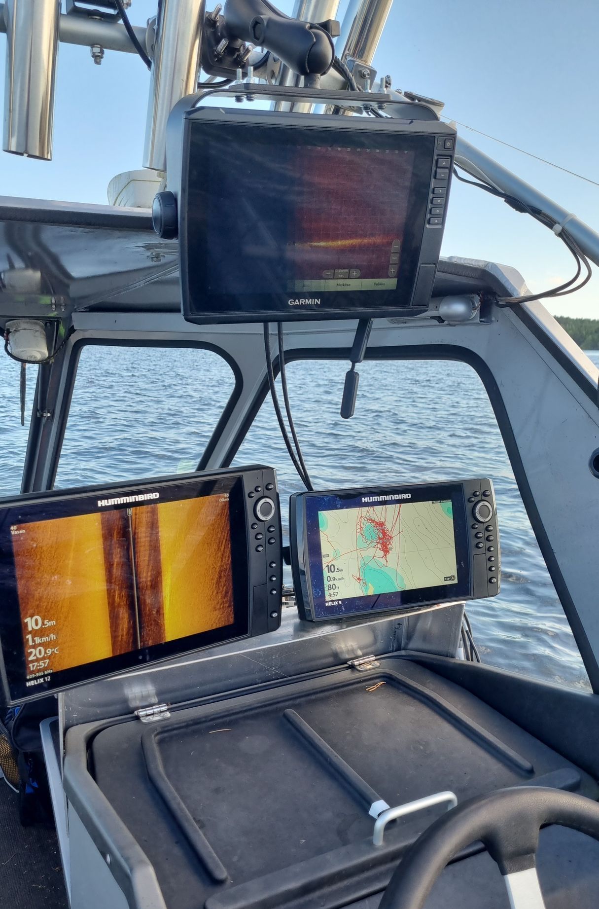 Boat cockpit with three marine navigation screens showing charts and sonar over open water