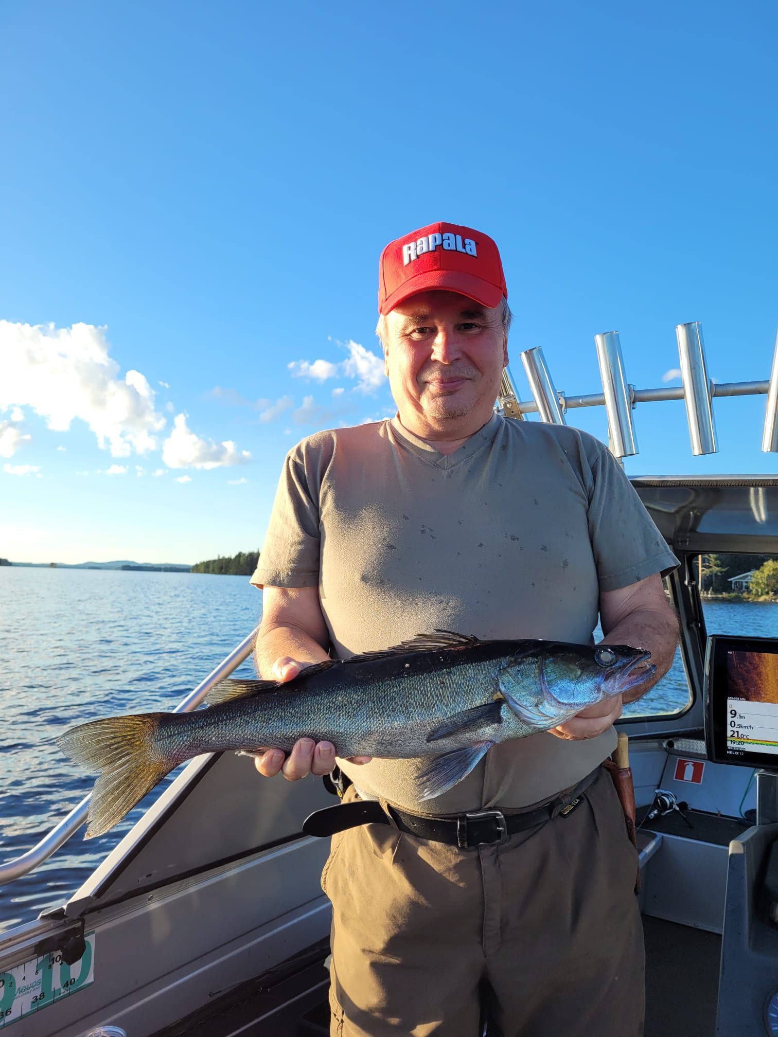 Man holding a pikeperch on a boat at sunset on calm water