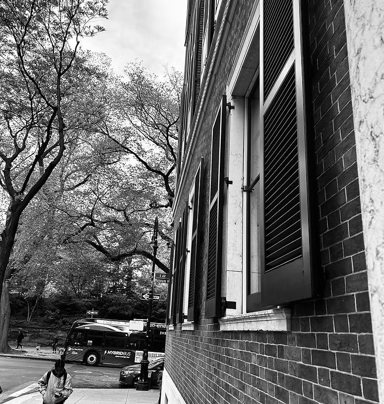 Black-and-white view of a brick building with windows, trees, and parked cars along a street