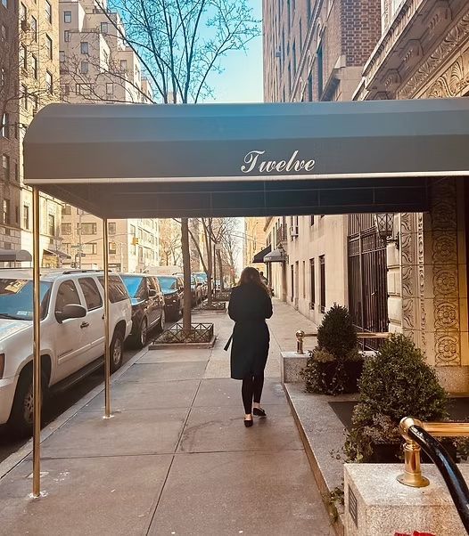 Person walks on city sidewalk under a dark awning labeled “Twelve.”