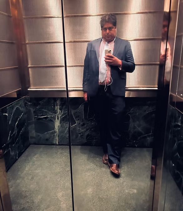 Person taking a mirror selfie in an elevator, wearing a suit and tie.